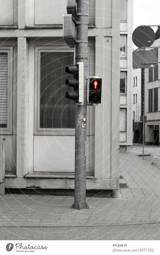 rote Ampel am Straßenrand in der Stadt Ampelmännchen Verkehrszeichen Fußgängerampel stillstehen Stillstand Innenstadt entsättigt Fassade Häuser Gehweg Ecke