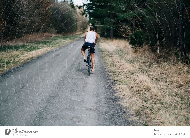 Junger Mann auf einem Fahrrad beim Fahrradfahren auf einer Straße durch den Wald Fahrradfahrer Freiheit Sommer Weg Sport Außenaufnahme Freizeit & Hobby