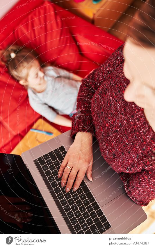 Mutter einer Frau, die während der COVID-19-Quarantäne von zu Hause aus per Video-Chat-Call-Stream-Online-Kurs Webinar auf einem Laptop durchführt, während ihre Tochter sich ein Video auf einem Tablet anschaut. Frau sitzt im Bett vor dem Computer und schaut auf den Bildschirm