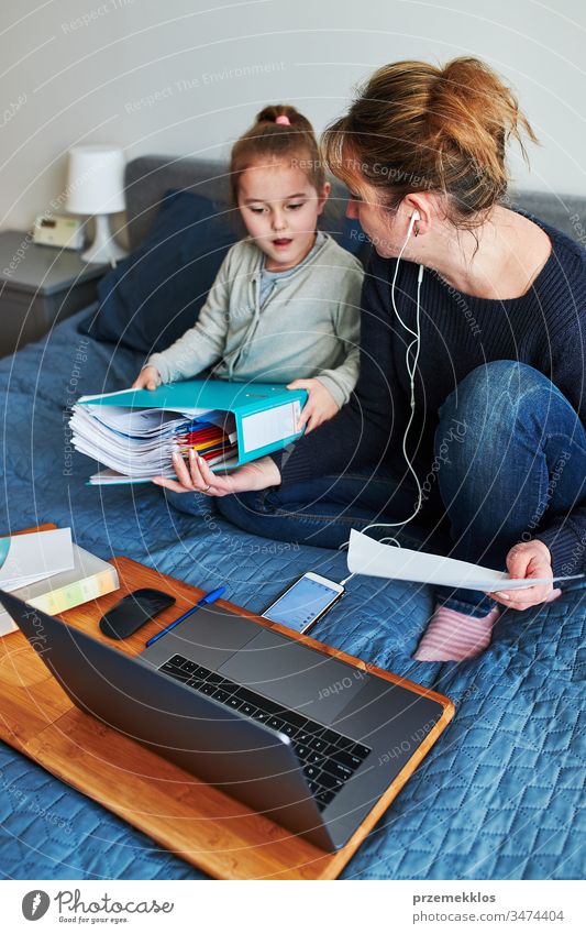 Die Mutter einer Frau, die während eines Video-Chat-Call-Stream-Online-Kurses auf einem Laptop von zu Hause aus ihren Job aus der Ferne erledigt, während ihre Tochter während der COVID-19-Quarantäne herumspielt. Frau sitzt im Bett vor dem Computer, schaut auf den Bildschirm und benutzt Kopfhörer