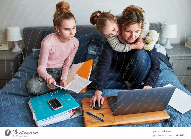 Mutter und Tochter von Frauen, die während der COVID-19-Quarantäne aus der Ferne lernen, indem sie während der Video-Chat-Call-Stream-Online-Kurs Webinar-Lektionen auf einem Laptop von zu Hause aus erledigen. Frauen sitzen im Bett vor dem Computer und schauen auf den Bildschirm