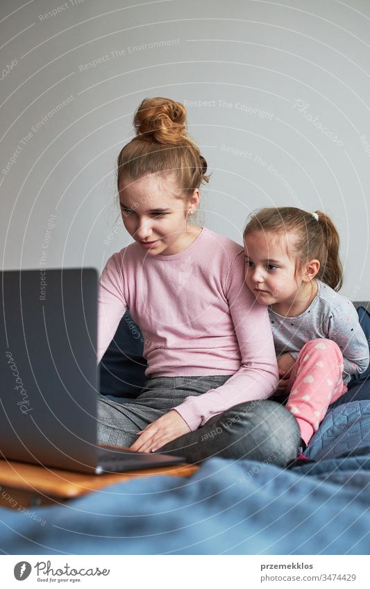 Teenagermädchen und ihre jüngere Schwester spielen beim Lernen am Laptop und verbringen während der COVID-19-Quarantäne Zeit miteinander zu Hause. Mädchen sitzen im Bett vor dem Computer