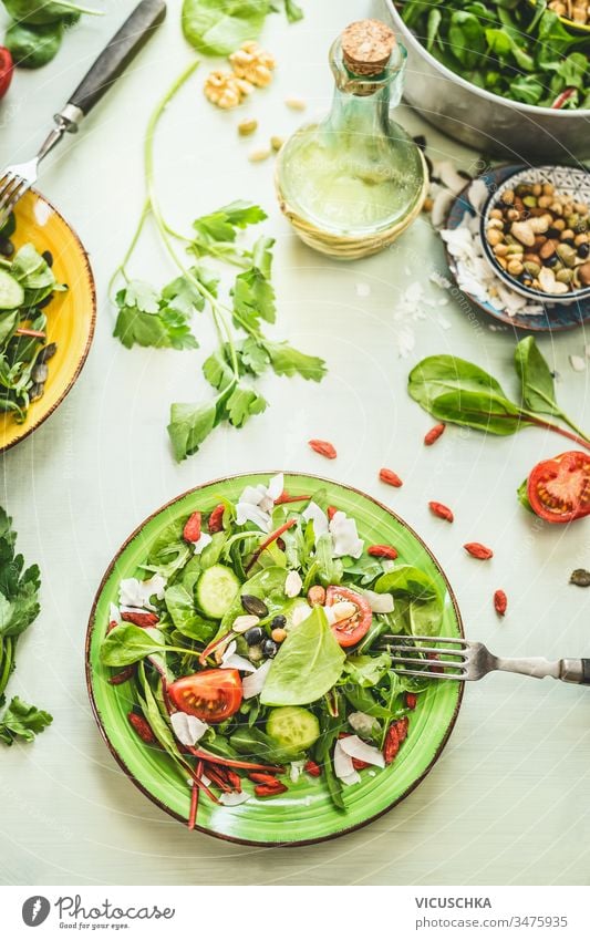 Gesunder frischer grüner Salatteller mit verschiedenen Samen und Beeren auf hellem Tischhintergrund mit Olivenöl und Zutaten. Ansicht von oben Gesundheit
