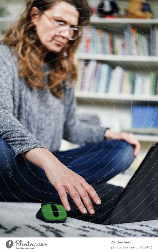 Frau sitzt im Homeoffice auf dem Boden und schaut konzentriert auf ihr Laptop genervt lesen Teppich Computer Notebook Maus Büro Business