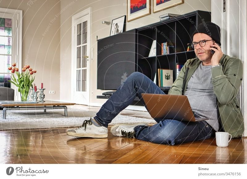 HomeOffice: der entspannte Mann sitzt wieder auf dem Boden vor seinem Notebook und freut sich auf sein Büro Wohnzimmer arbeiten von zu Hause Heimarbeitsplatz