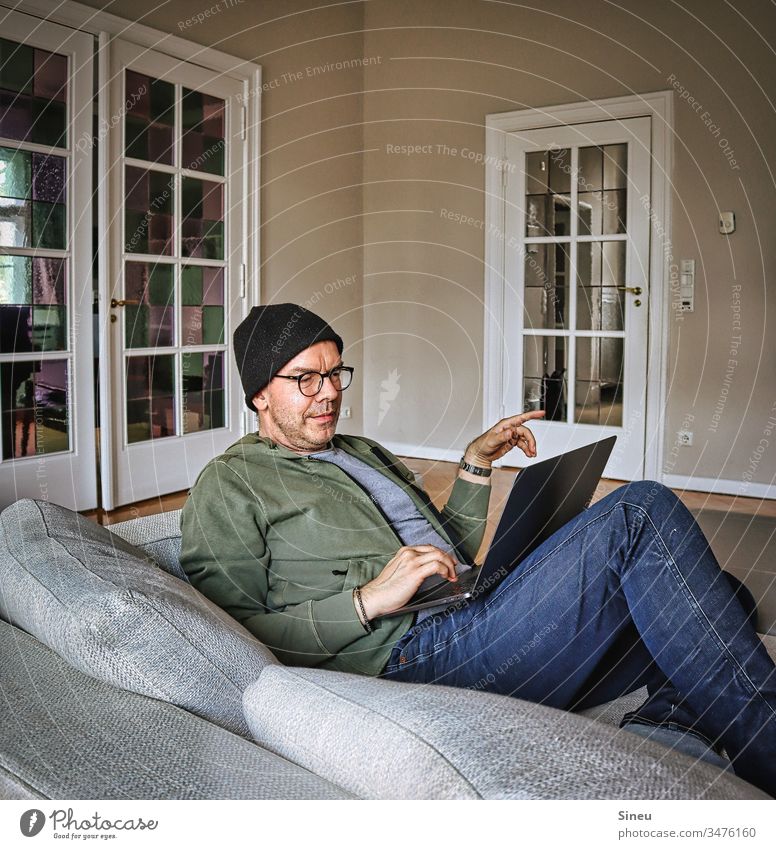 HomeOffice: immer noch entspannter Mann liegt jetzt mit seinem Notebook wieder auf dem Sofa und arbeitet Wohnzimmer Heimarbeitsplatz ein Mann alleine
