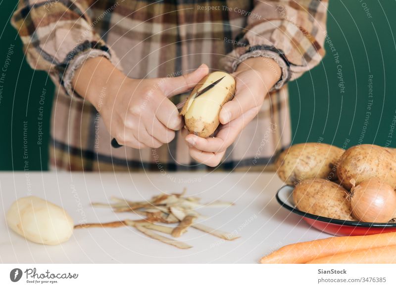 Frau schält in ihrer Küche Kartoffeln auf weißem Marmor ab, um ihr Essen zuzubereiten. sich[Akk] schälen Gemüse Veganer heimwärts peel-off angeblättert Karotten