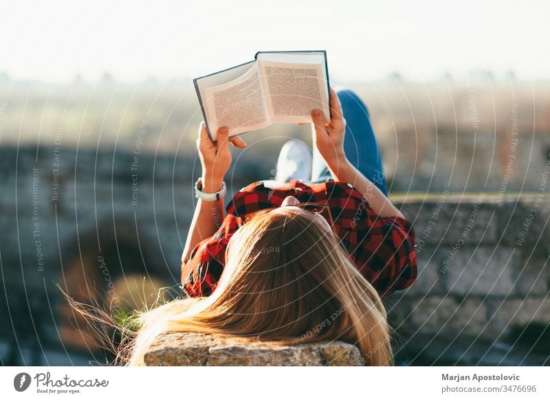 Junge Frau liest ein Buch im Freien jung lesen außerhalb Freude studierend Schüler genießend Lifestyle Frühling Sommer Lügen Freizeit Mädchen Menschen Person