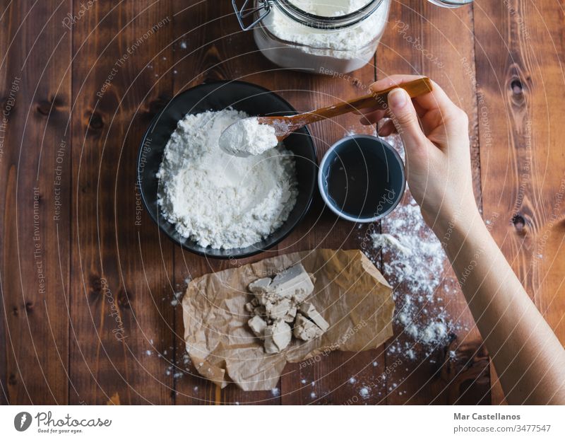 Eine Frauenhand fügt Mehl hinzu, um Sauerteig herzustellen. Konzept einer Bäckerei. Teigwaren kneten Löffel Hefe Verarbeitung Glasgefäß selbstgemacht Holzboden