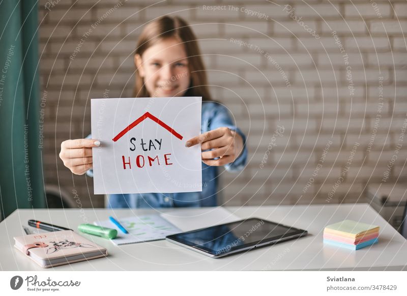 Ein schönes junges Mädchen hält ein Schild mit der Aufschrift "Bleiben Sie zu Hause". Das Mädchen empfiehlt, während der Quarantäne zu Hause zu bleiben. Selbstisolation, soziale Distanz