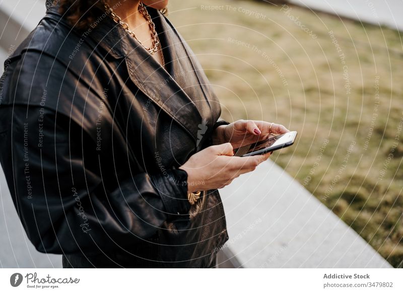 Trendige Managerin benutzt Smartphone im Gartenbogen Geschäftsfrau benutzend Park retro Arbeit Leder Jacke cool Outfit jung Arbeitsweg Stil Frau Kommunizieren
