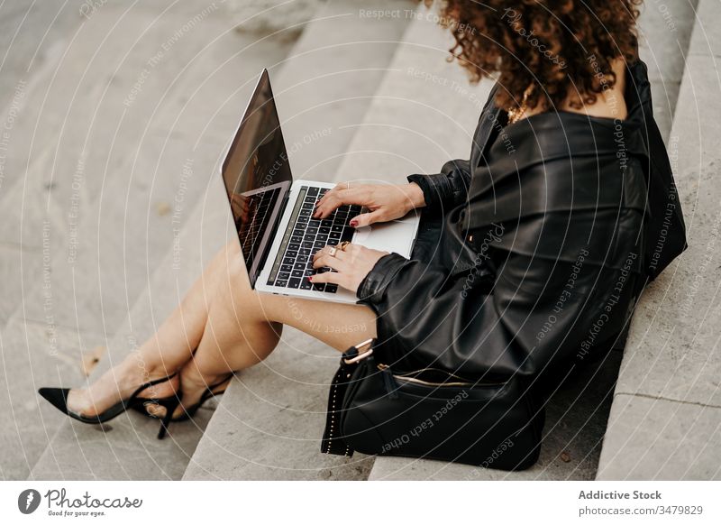 Schicke trendige Frau in Lederkombi beim Stöbern am Laptop auf der Treppe Geschäftsfrau benutzend Projekt Straße sitzen Tippen Großstadt retro Outfit Browsen