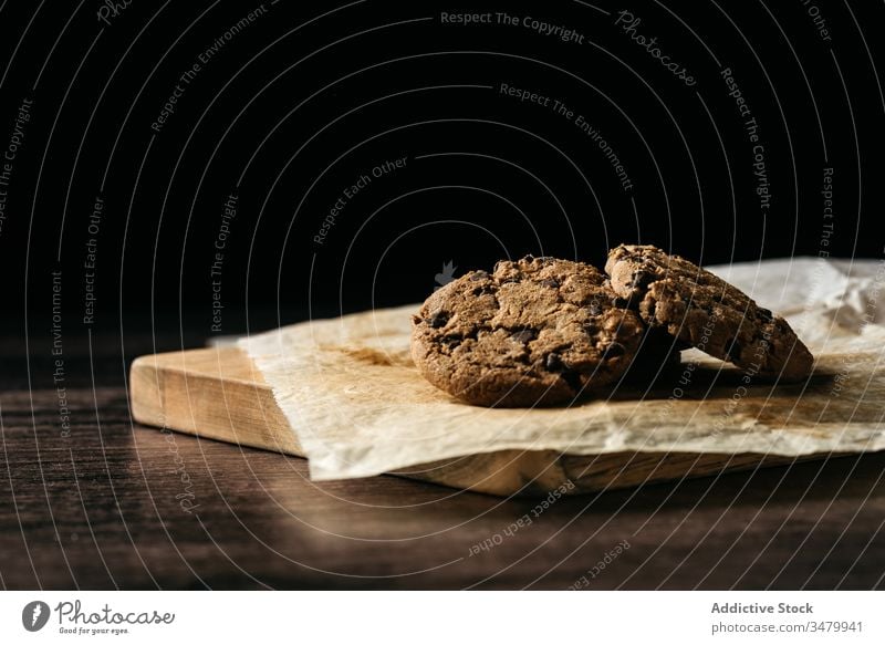 Leckere Schokoladenkekse auf Holztisch Keks hölzern gebacken Gebäck Biskuit süß Papier Lebensmittel Dessert dunkel geschmackvoll selbstgemacht Snack frisch