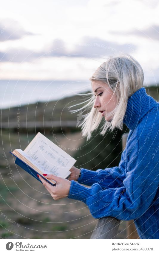 Junge Frau liest Buch am Meer MEER Zaun Strand ruhen lesen jung blau genießen Poesie Pullover Natur sich[Akk] entspannen hölzern Stil allein modern trendy blond