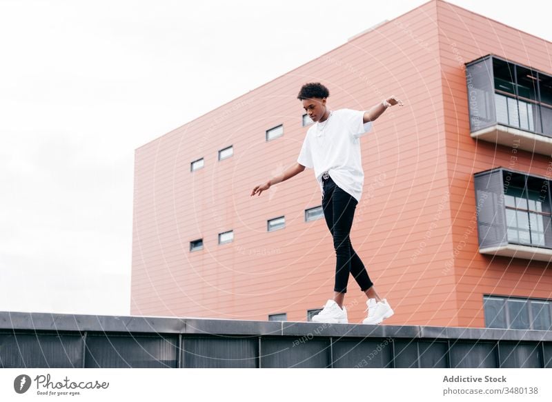 Modischer ethnischer Mann stellt sich gegen modernes Bauen Streetstyle Mode trendy cool urban Gebäude jung Großstadt selbstbewusst Afroamerikaner schwarz