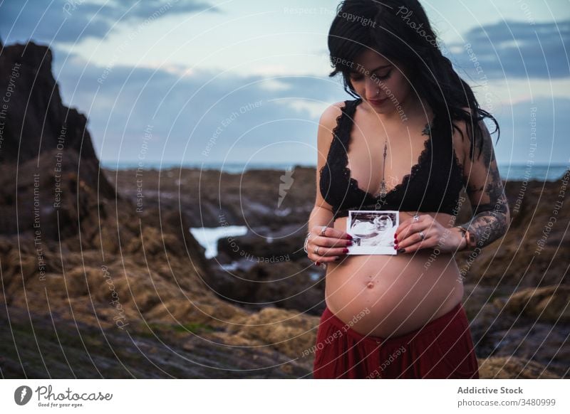 Liebende stilvolle Schwangere mit Sonogramm-Bild am Ufer Frau Natur schwanger vorwegnehmen Eltern erwarten Freiheit Harmonie Himmel sinnlich Stil Küste reisen