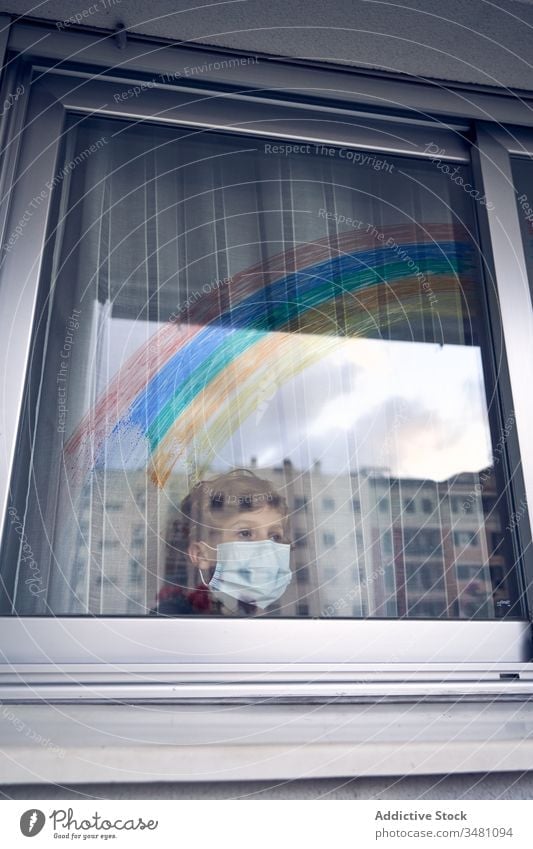 Junge hinter Fenster während der Quarantäne Mundschutz medizinisch Regenbogen farbenfroh heimwärts Krankenhaus Stirnrunzeln Pandemie Coronavirus Bund 19 Kind