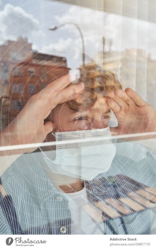 Junge hinter Fenster während der Quarantäne Mundschutz medizinisch heimwärts Stirnrunzeln Pandemie Coronavirus Bund 19 Kind Kindheit traurig unglücklich Hygiene
