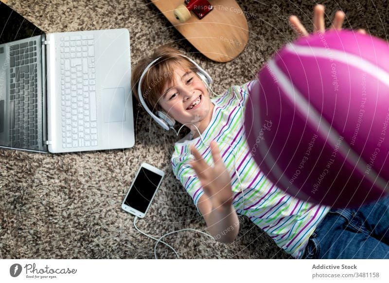 Glücklicher Junge hat Spaß zu Hause Kind Apparatur heimwärts Musik spielen Ball werfen räkeln Kopfhörer Smartphone sich[Akk] übergeben heiter zuhören Lügen