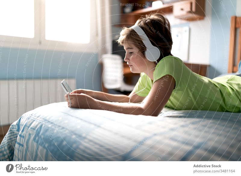 Fröhliches Kind sieht Film auf Tablett im Schlafzimmer Apparatur Tablette heimwärts zuschauen Kopfhörer heiter Junge benutzend Lachen online zuhören Internet