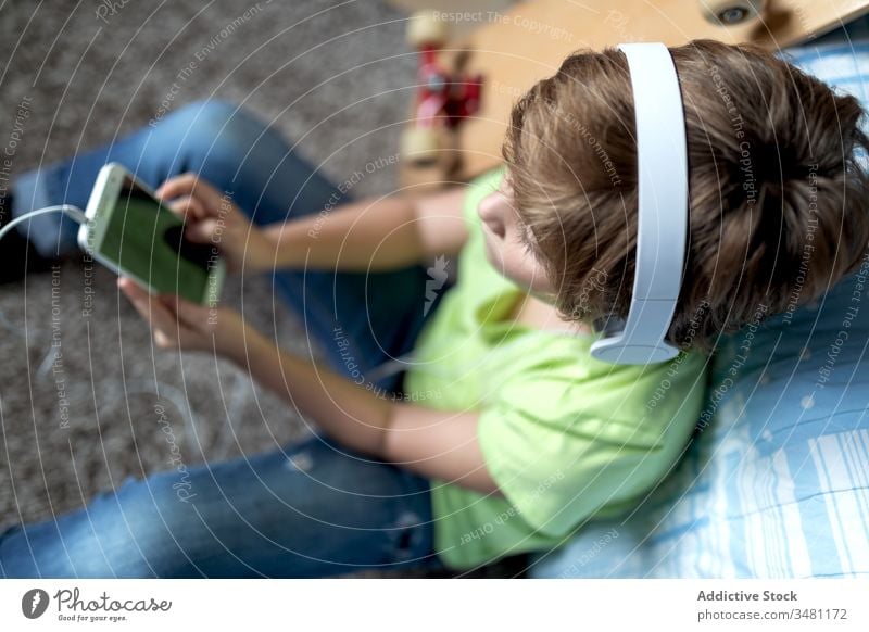 Kind mit Kopfhörern, das zu Hause ein Smartphone benutzt Apparatur heimwärts Junge benutzend Talkrunde Gerät online zuhören Internet Lifestyle modern Mobile