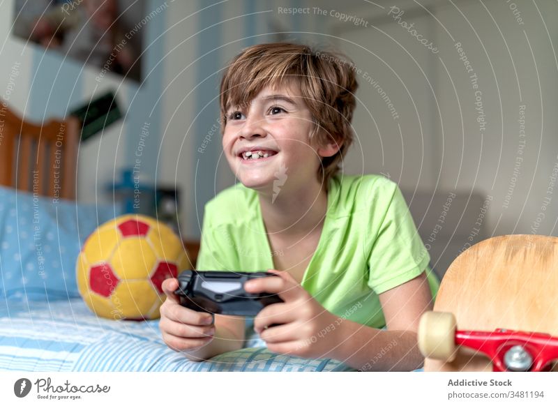 Glücklicher Junge spielt Videospiel im Schlafzimmer Kind Spaß spielen Gamepad Gerät aufgeregt Apparatur heimwärts Lügen heiter benutzend Konsole Bett Lifestyle