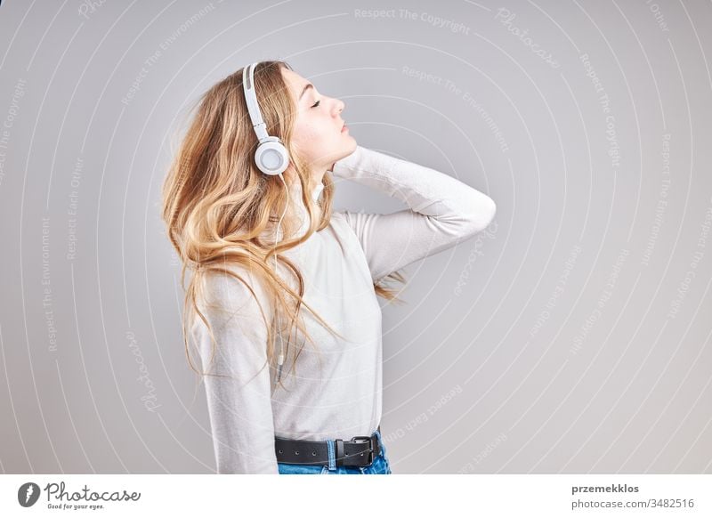 Junge Frau Mädchen, die Musik hört, die Inhalte streamt und Spaß beim Ansehen von Videos hat, Video-Chat genießt und sich mit Freunden unterhält, die Gesten machen Gesichter mit Smartphone-Ohrhörern Kopfhörer stehen über einfachem grauen Hintergrund