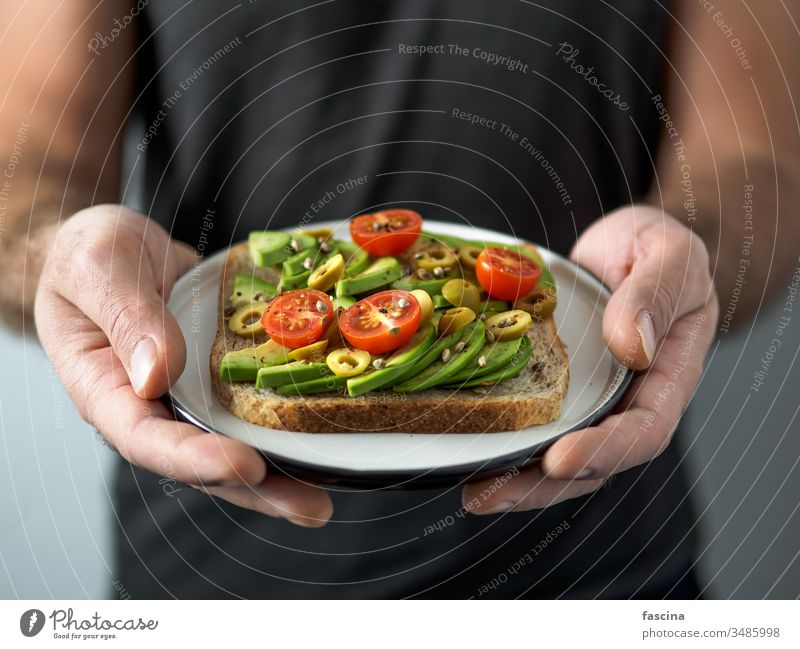 Veganes Sandwich mit Avocado in Männerhänden Belegtes Brot Veganer Hand Zuprosten Veggie Avocado-Toast Teller pflanzlich verzehrfertig Ideen Gesundheit