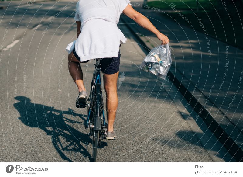 Ein Mann im Sommer auf einem Fahrrad mit einer Tüte voller Metallmüll beim Müll wegbringen; Recycling, Mülltrennung Fahrradfahrer Fahrradfahren Radfahrer Aktion