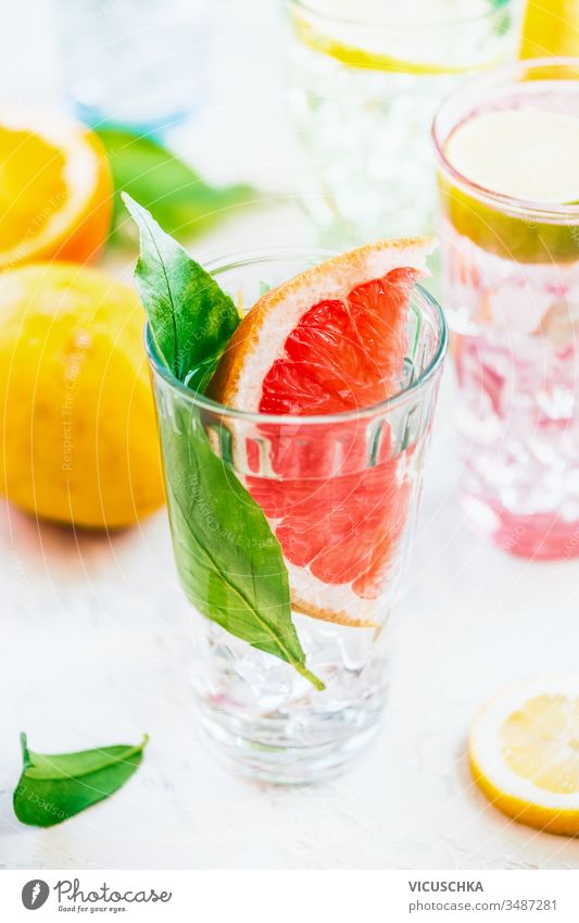 Sommer-Erfrischungsgetränk mit Grapefruitscheiben und grünen Blättern im Sonnenlicht auf weißem Tisch , Nahaufnahme. Aufgegossenes Entgiftungswasser. Vitamin C. Antioxidans