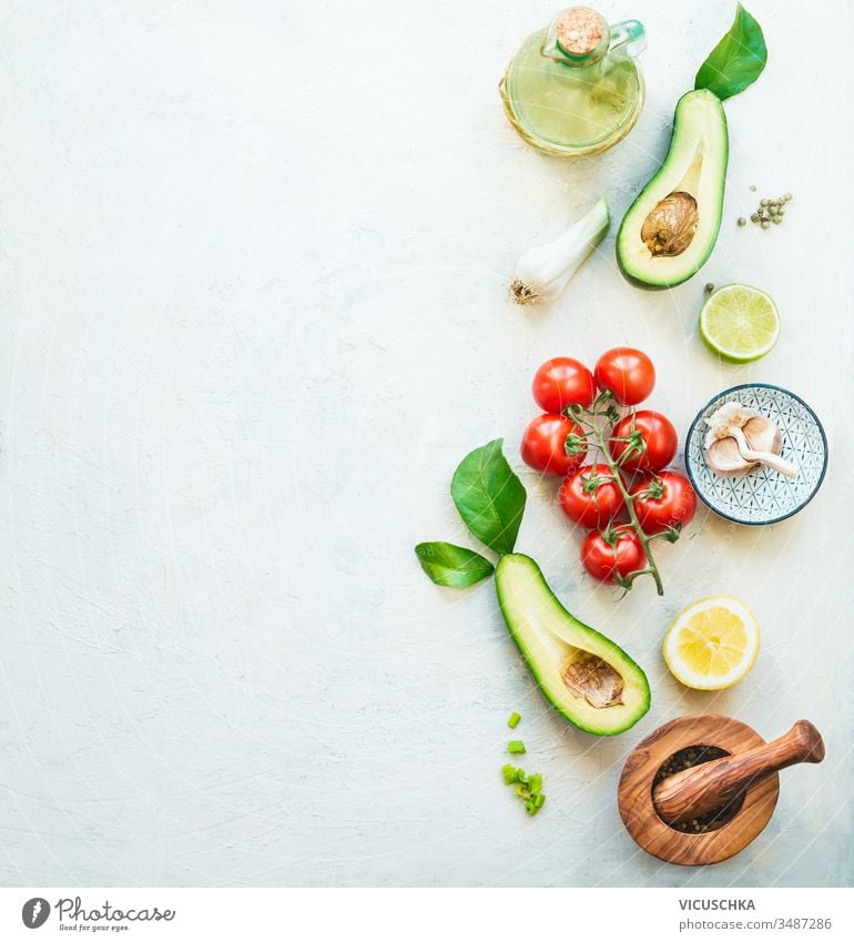 Lebensmittelhintergrund mit frischen Salatzutaten: Avocado, Tomaten, Zitrone, Knoblauch und Olivenöl zur schmackhaften Salatzubereitung, Draufsicht. Gesundes Essen.  Vegetarisches Mittagessen oder Snack. Grenze