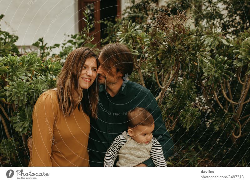 Liebenswertes Paar steht zusammen, während der Mann ihren kleinen Sohn hält alternativ Indie Hipster Lächeln Frau Papa Eltern Porträt im Freien Garten