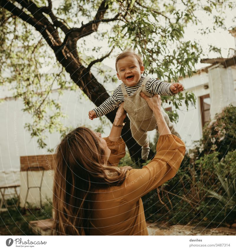 Mutter hält ihren kleinen Sohn in die Luft und das Baby lacht. Spielen Erwachsener Fliege Waffen Werfen genießend Elternschaft blond Garten Baum Leben Frau