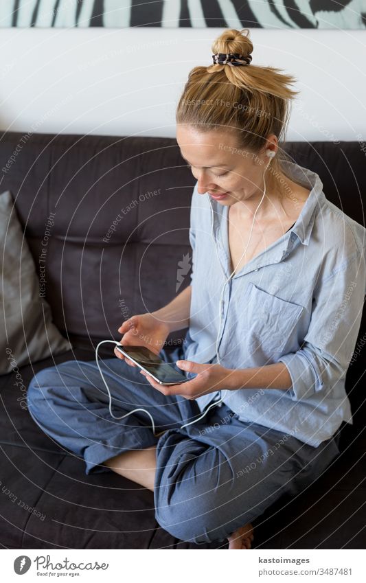 Frau zu Hause, die sich auf der Couch entspannt und während der Coronavirus-Pandemie soziale Medien am Telefon für Video-Chats mit ihren Lieben nutzt. Zu Hause bleiben, sozial distanzierender Lebensstil.