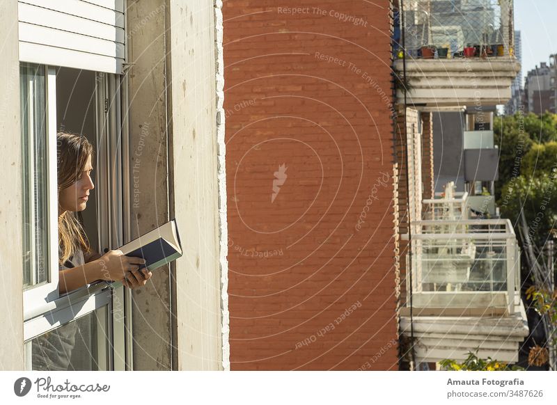 Frau in den Fenstern während der Quarantäne beim Lesen eines Buches Appartement schön blind Windstille Teppich Stuhl Komfort bequem Corona-Virus Bund 19