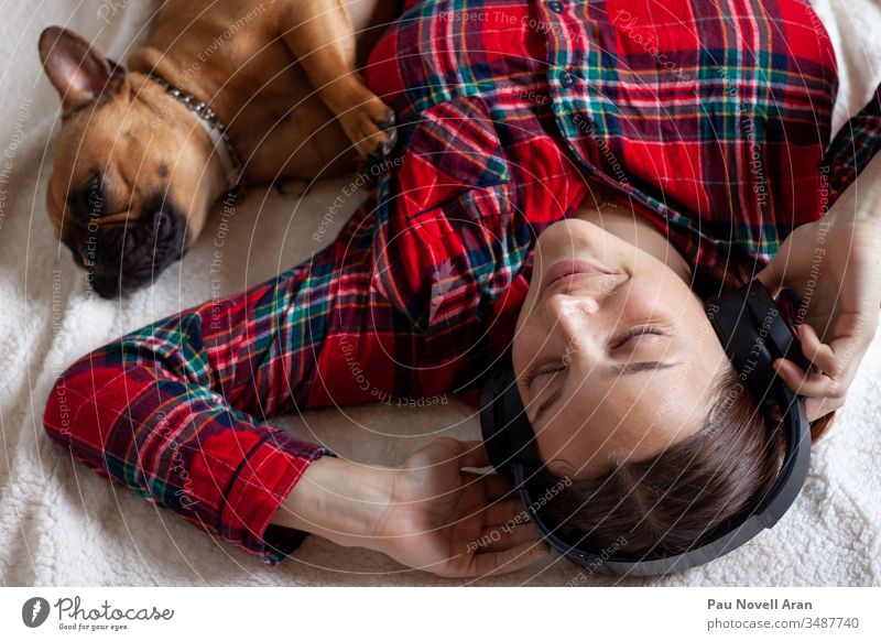 Französische Bulldogge mit junger Frau mit Kopfhörern, die lächelnd auf der Couch liegt französische Bulldogge Hund LAZY Klang Vorstellungskraft Menschen Raum