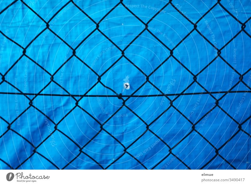 Maschendrahtzaun vor blauer PVC-Plane mit kleinem Loch Sichtschutz Schutz Abgrenzung Guckloch Zaun Begrenzung Grenze Drahtzaun Barriere Sicherheit gefangen