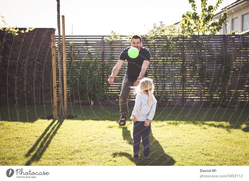 Kind und Vater spielen im Garten mit einem Ball werfen und fangen Mädchen Mann Tochter Spielen beschäftigen spass lachen Freude fliegen Schatten Sonnenlicht