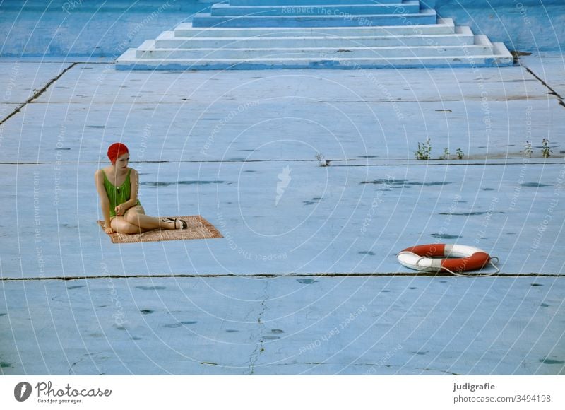 Das Mädchen mit der schönen roten Badekappe und dem grünem Badeanzug sitzt in einem leeren Schwimmbecken und schaut auf einen Rettungsring. Eine Sommerliebe.