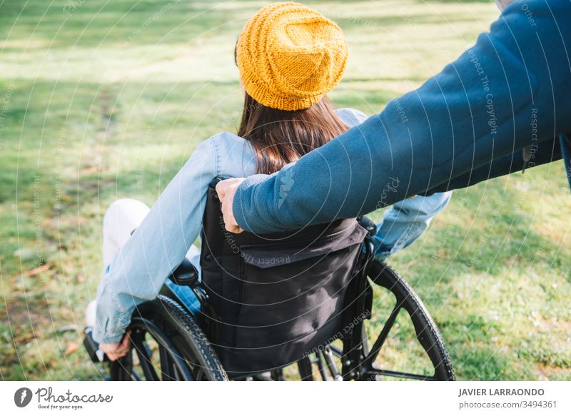 Freiwilliger schiebt den Rollstuhl eines jungen behinderten Mädchens in einem ga Zugänglichkeit Behinderung Frau Fröhlichkeit Optimismus Mobilität Behinderte