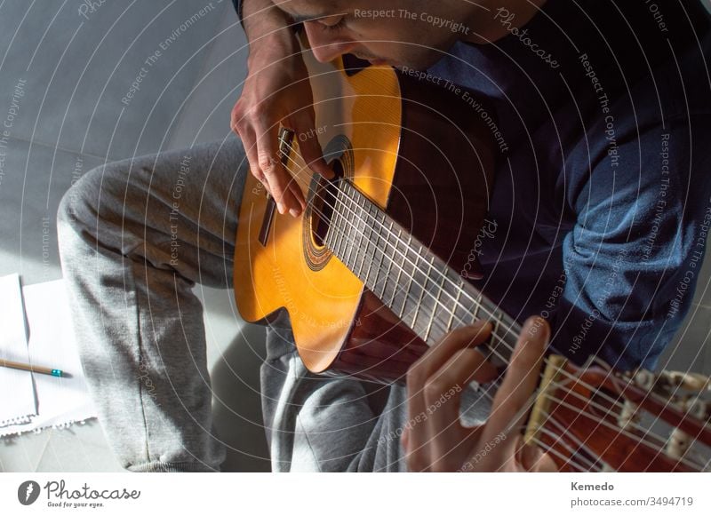 Draufsicht auf einen jungen Mann, der zu Hause Gitarre spielt und Musik komponiert. Lässiger Mann, der auf dem Boden sitzt und Gitarre lernt. spielen lernen
