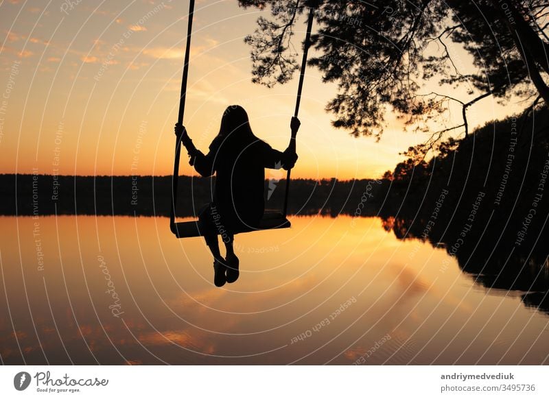 romantische junge Frau auf einer Schaukel über dem See bei Sonnenuntergang. Junges reisendes Mädchen auf der Schaukel sitzend in schöner Natur, Blick auf den See