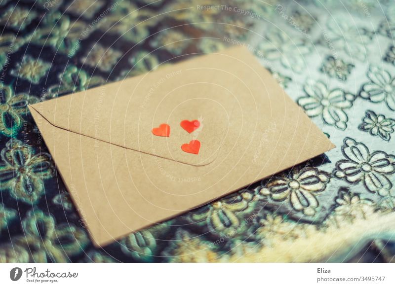 Ein mit drei roten Herzen dekorierter Briefumschlag, der auf einem ornamentalem Hintergrund liegt; Liebesbrief Muttertag Geschenk Kommunikation Nachricht