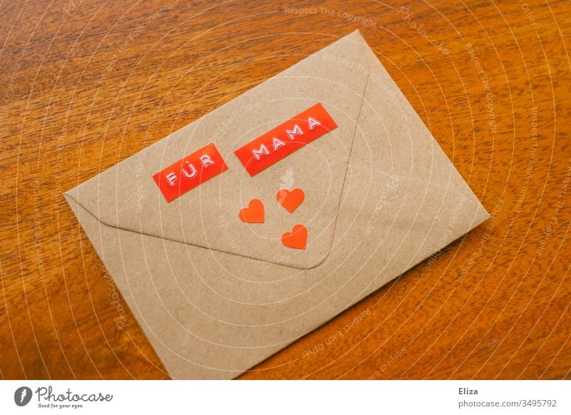 Ein Briefumschlag auf dem Für Mama steht mit drei roten Herzen dekoriert auf einem Untergrund aus Holz; Nachricht Geschenk an die Mutter zu Muttertag Liebe