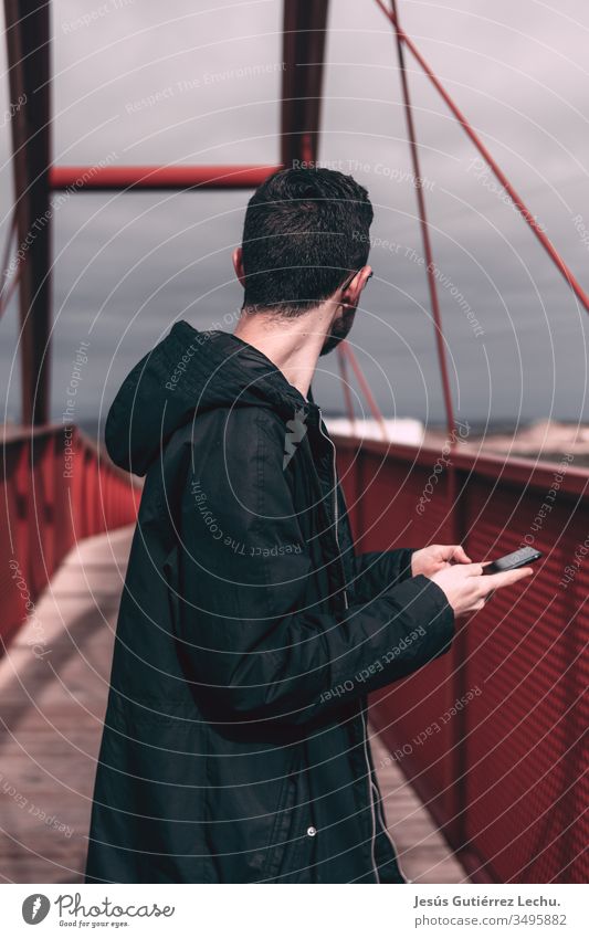 Mann in schwarzem Mantel, der ein Mobiltelefon auf einer roten Brücke hält Tag Stadt Brückenbau Ferien & Urlaub & Reisen Architektur Brückenpfeiler Himmel