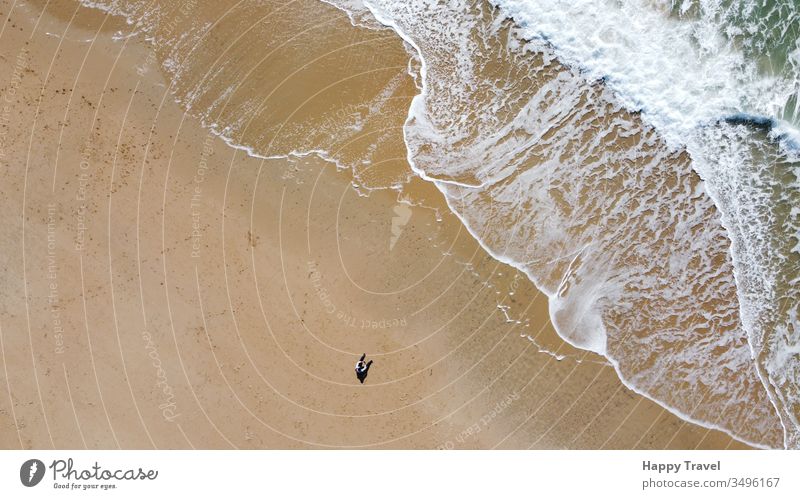 Luftaufnahme eines Sandstrandes. Ein Mann sitzt auf dem Sandstrand und schaut auf die Welle, die sich in seiner Nähe bricht. Sonniger Tag sonniger Tag Strand
