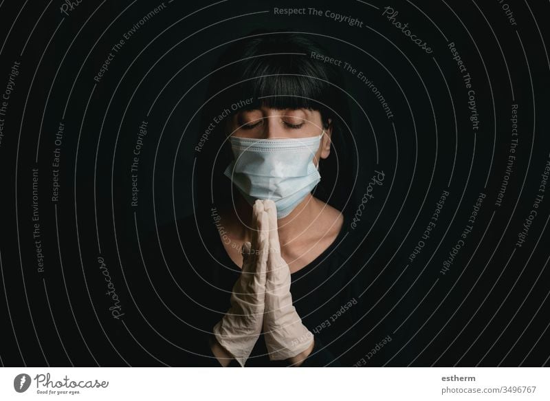 junge Frau, die eine medizinische Maske für Coronavirus trägt, mit zusammengeklappten Händen betend covid-19 Junge Frau 2019-ncov Virus Seuche Pandemie