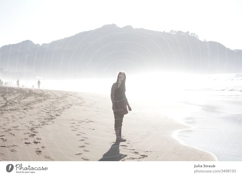 Frau läuft am Strand spazieren Sandstrand Meer Silhouette Gegenlicht Fußspur Spanien Zarautz Baskenland Rückblick Wärme diesig Wasser Barfuß Wellen Urlaub Füße