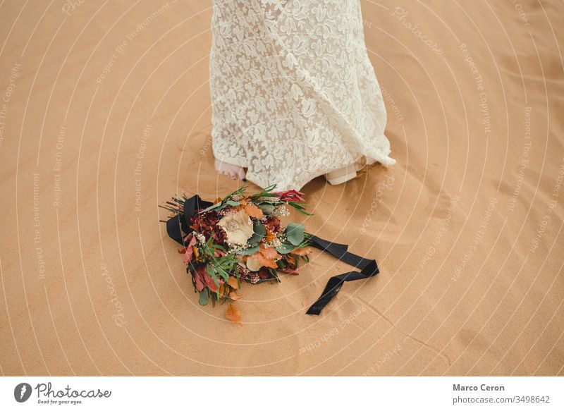 Brautstrauß, der neben den Füßen der Braut auf dem Sand liegt. Blume Frau Blumenstrauß außerhalb Kleid im Freien Dekoration & Verzierung Ordnung geblümt