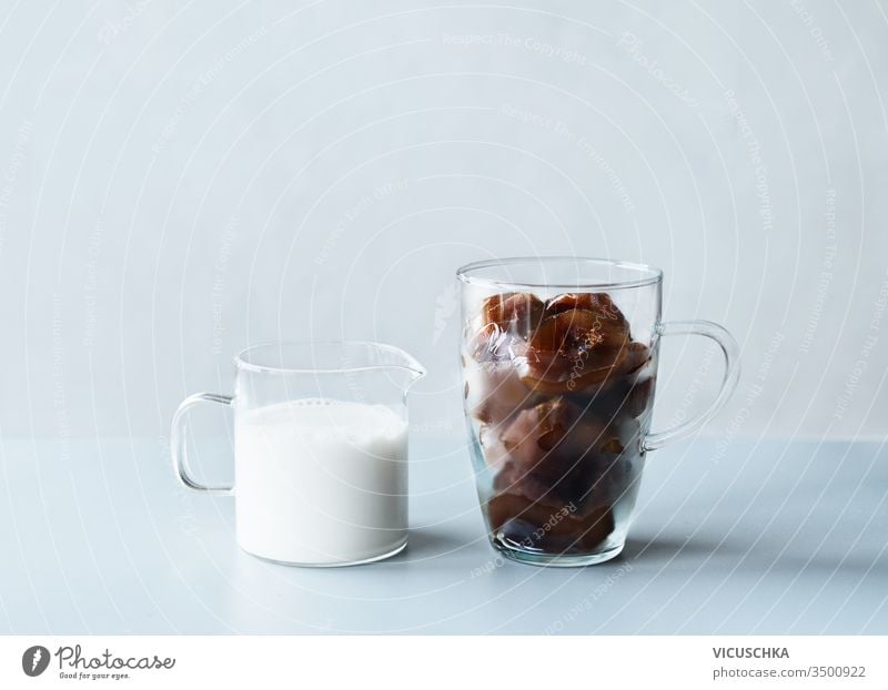 Kaffee-Eiswürfel in Glasbecher und Kännchen mit Sahne oder veganer Milch auf grauem Tisch im Wandhintergrund. Erfrischende Sommergetränke machen Zutaten Becher